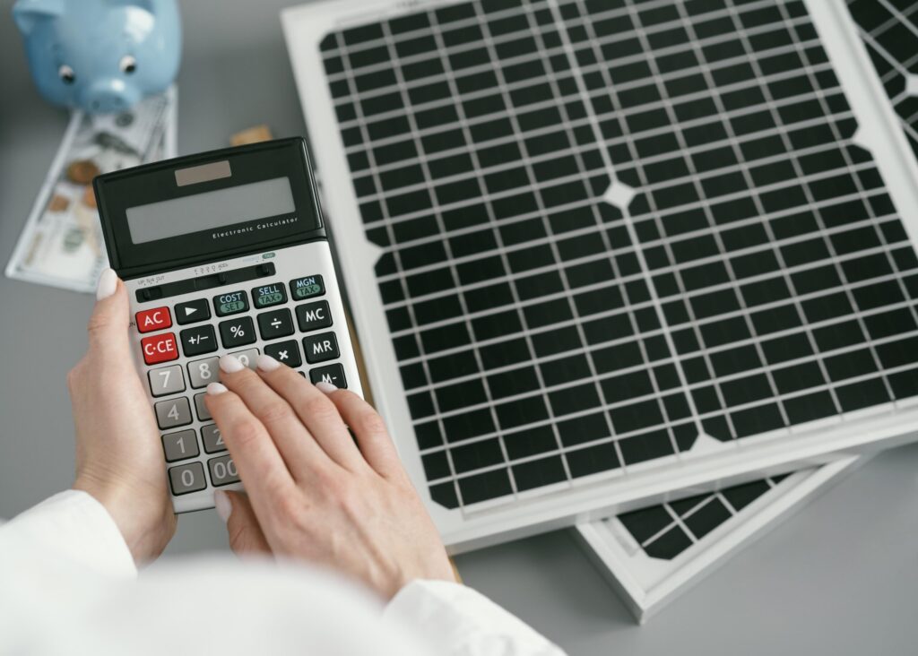 Calculator placed next to solar panels illustrating cost comparison between EMI and upfront payment when choosing the best solar company in Kerala.
