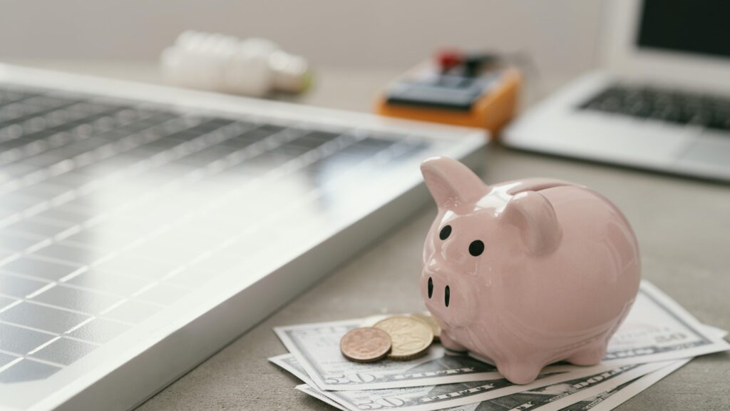 Piggy bank with cash placed beside a solar panel, representing savings and financing options offered by the best solar company in Kerala.
